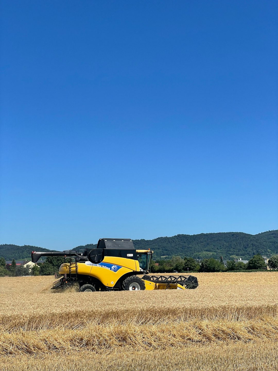 Un agriculteur teste un semoir attaché à un tracteur dans un champ fraîchement labouré, sous un ciel bleu clair.