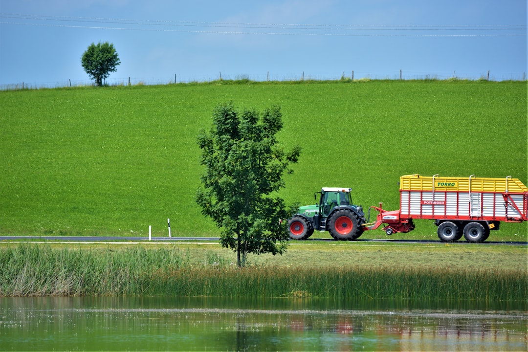 Paysage agricole vallonné de Bretagne avec un tracteur rouge travaillant dans un champ vert sous un ciel légèrement nuageux.
