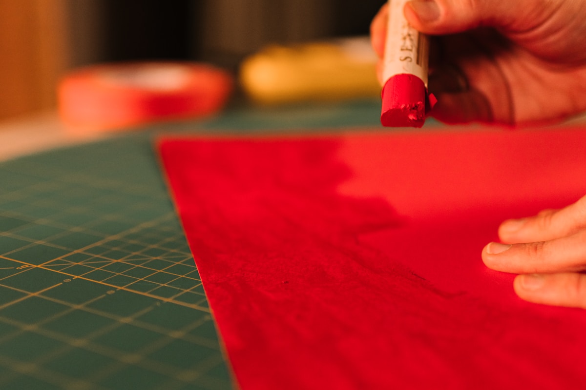 Hand applying glue stick to red paper.
