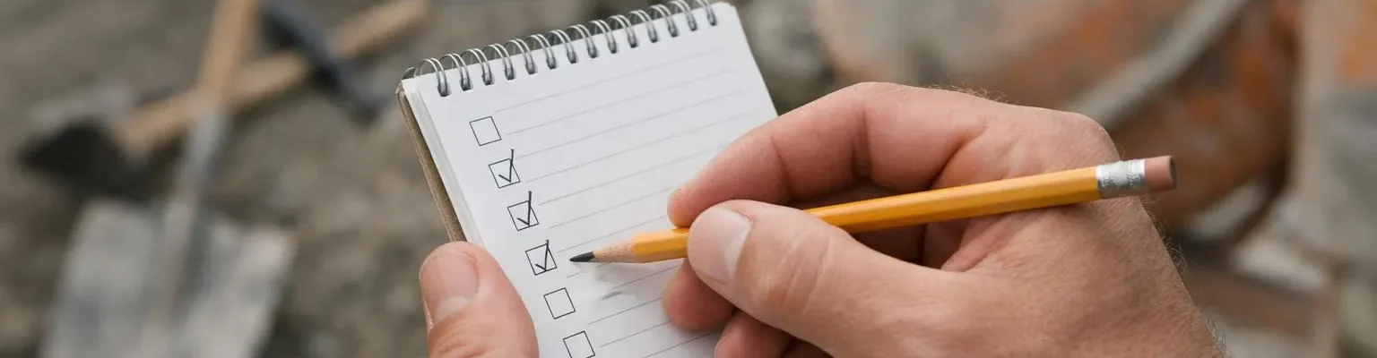 "Main tenant un cahier et un crayon sur un chantier BTP, évaluation matériel"