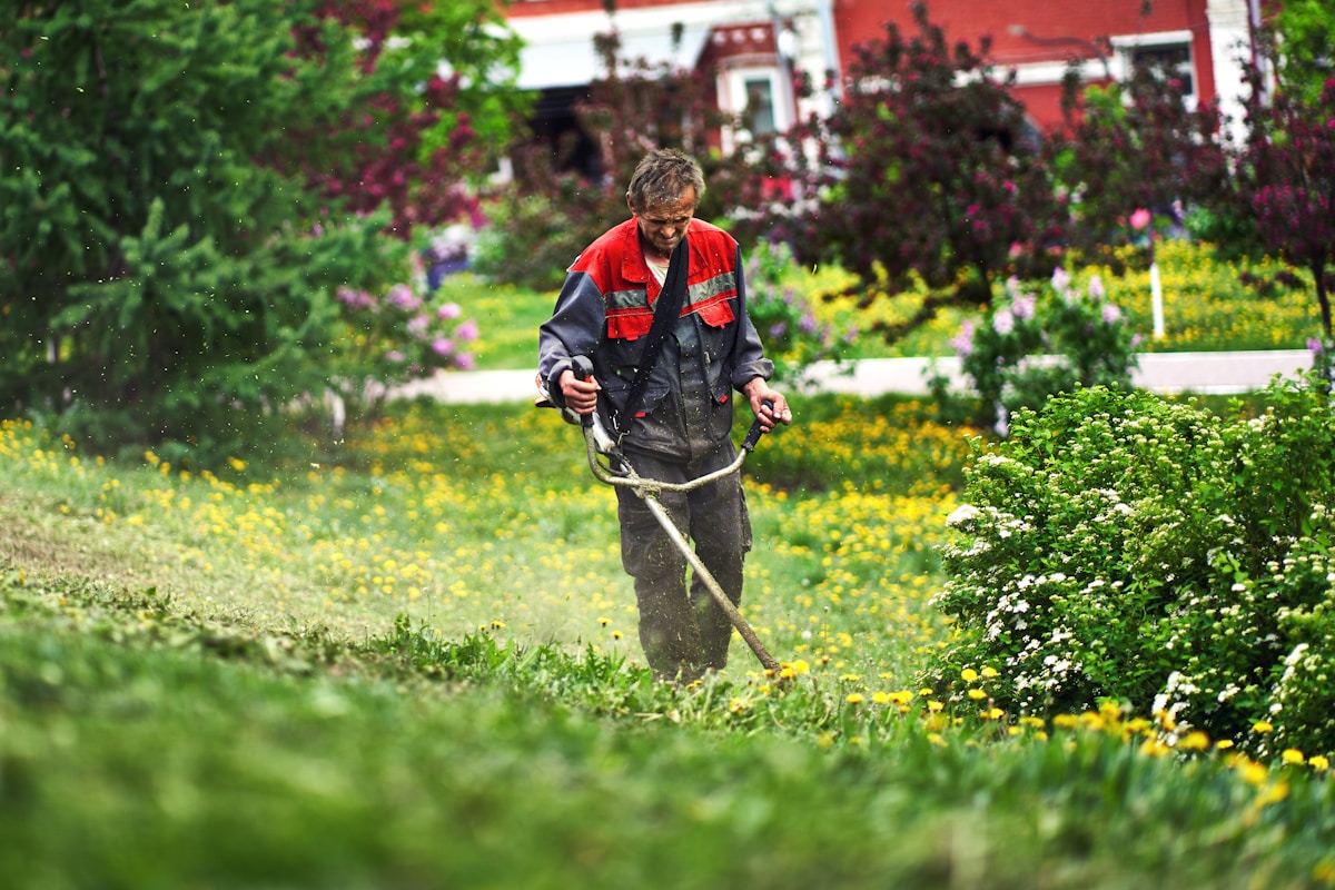 Jardinier en tenue de travail tondant la pelouse dans un jardin fleuri.