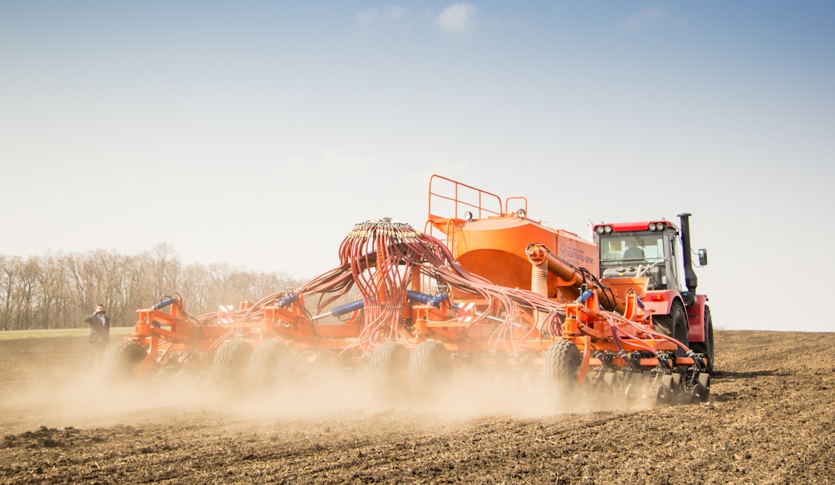 Tracteur agricole orange labourant un champ poussiéreux.