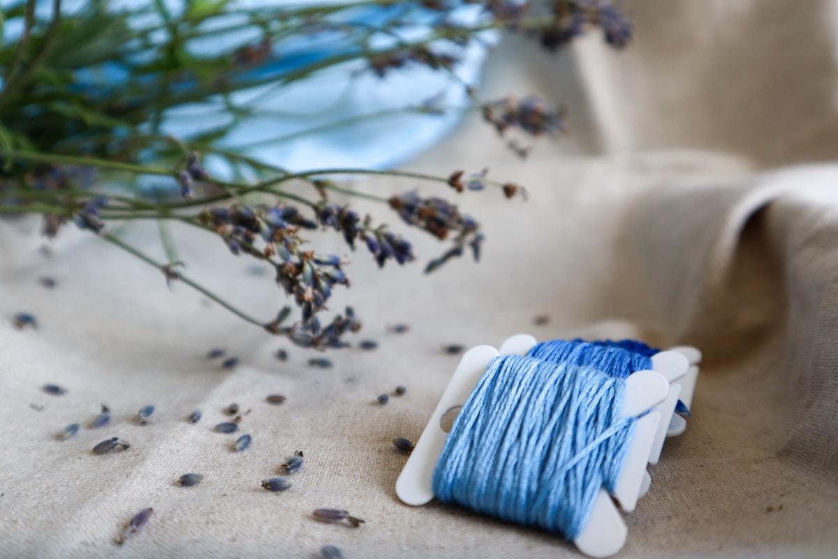 Bobine de fil bleu entourée de branches de lavande.