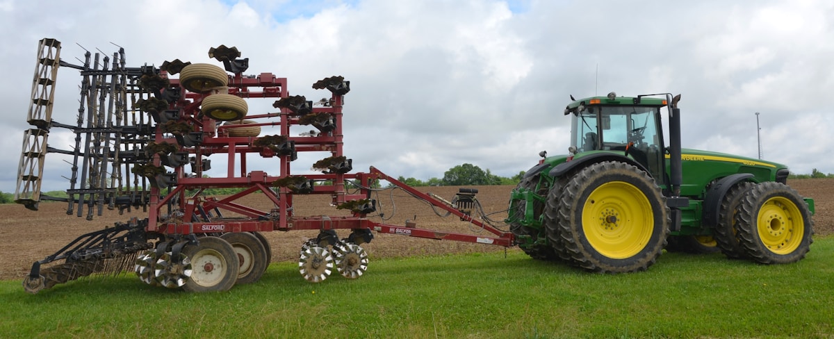 Tracteur vert tirant un équipement agricole complexe dans un champ.