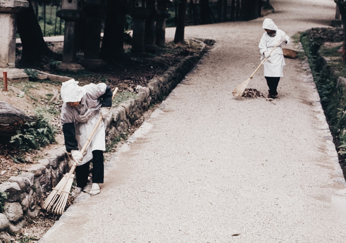 Deux personnes en vêtements blancs balayant un chemin de terre.