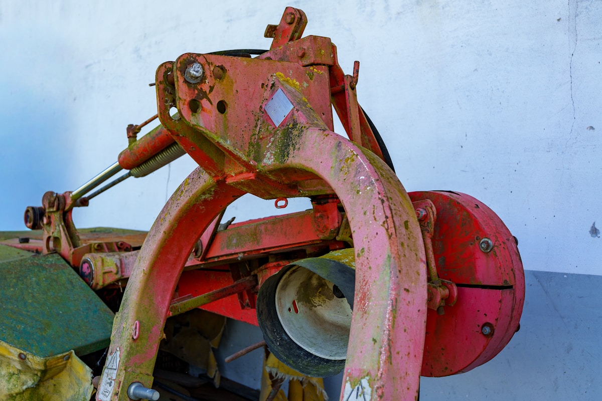 Vieux tracteur agricole rouillé et désuet, avec des pièces mécaniques apparentes.