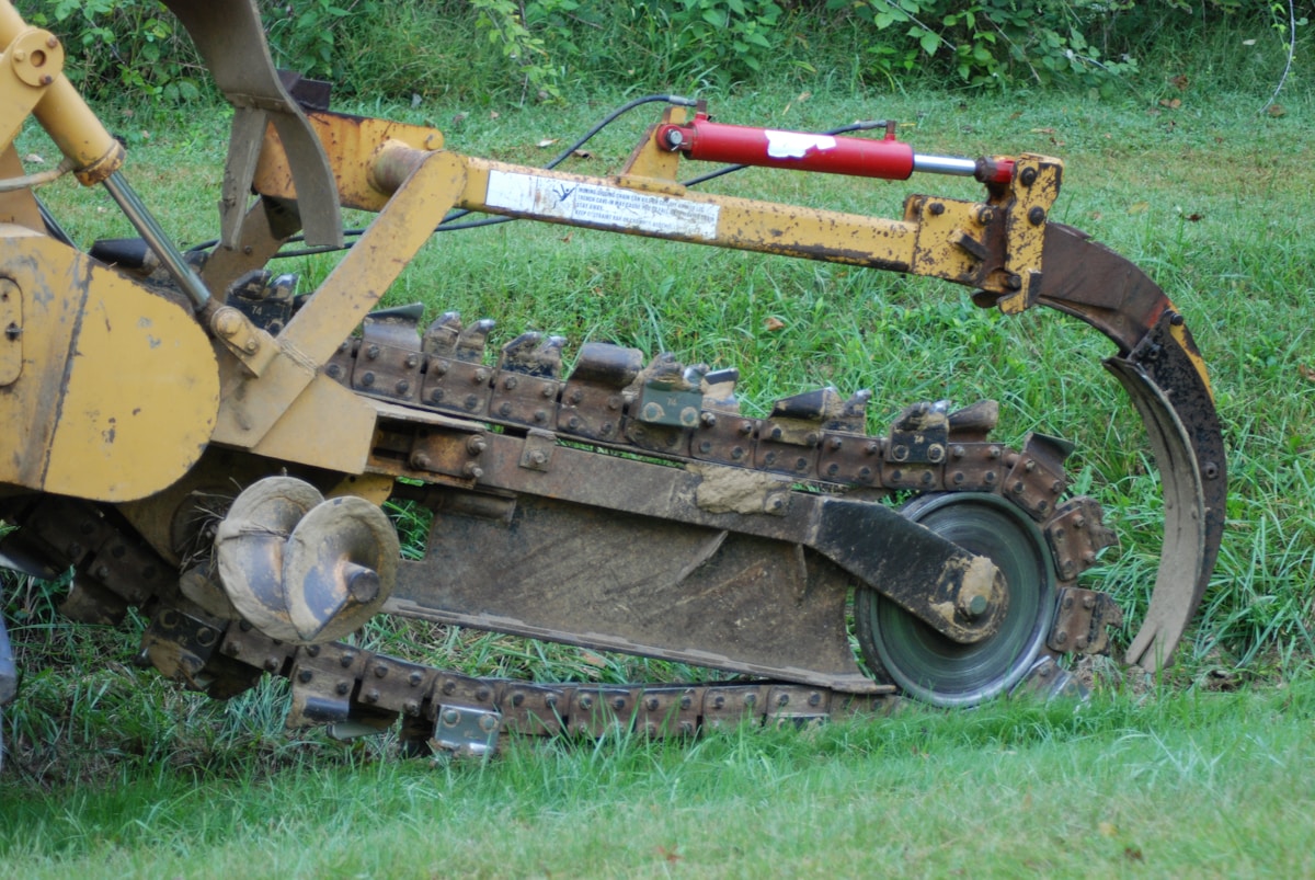 Tracteur agricole jaune et rouillé avec accessoire sur l'herbe verte.