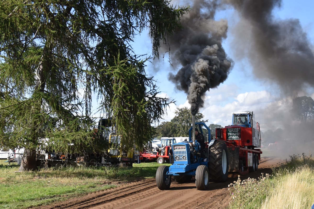 Tracteurs agricoles sur une route de campagne avec un panache de fumée noire à l'arrière-plan.