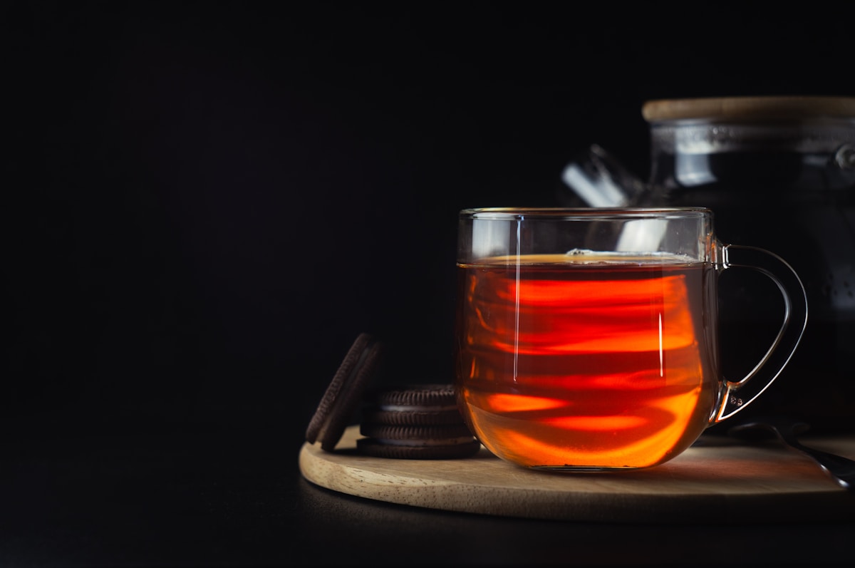Tasse de thé noir chaud sur plateau en bois sombre.