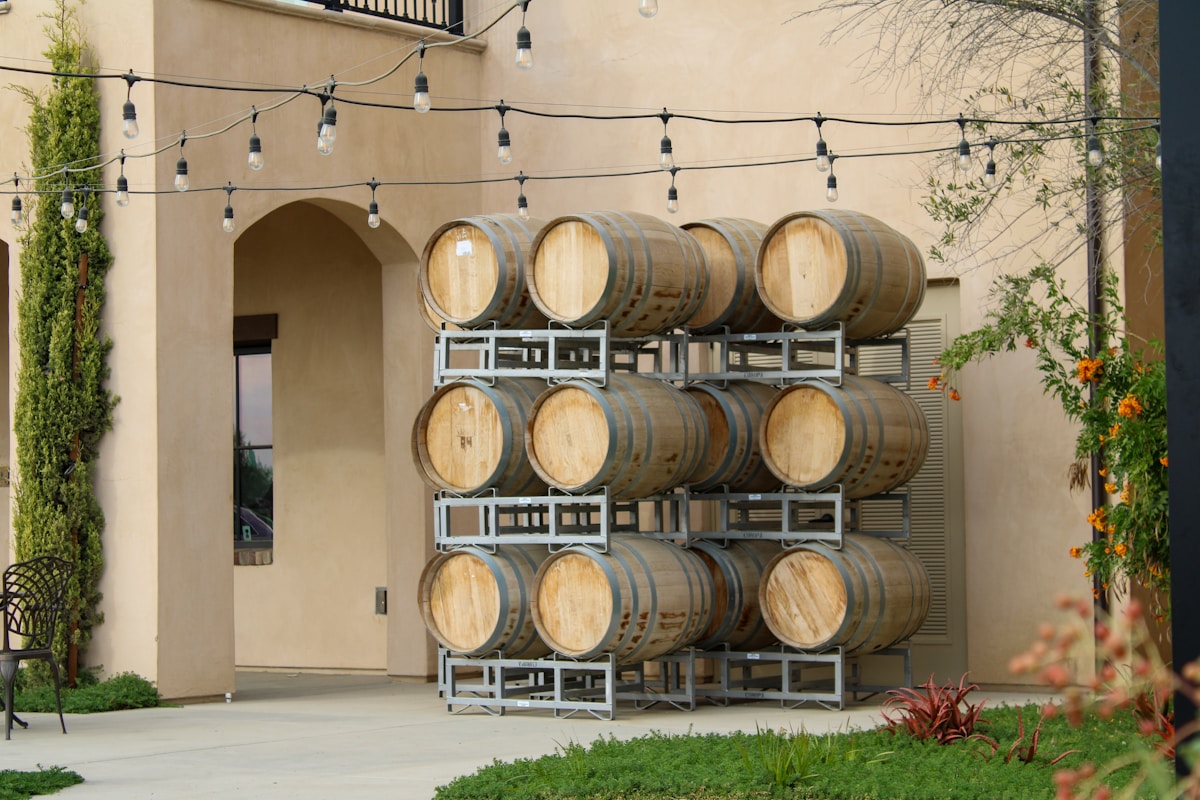 Rangées de fûts de vin dans une cour avec guirlandes lumineuses.