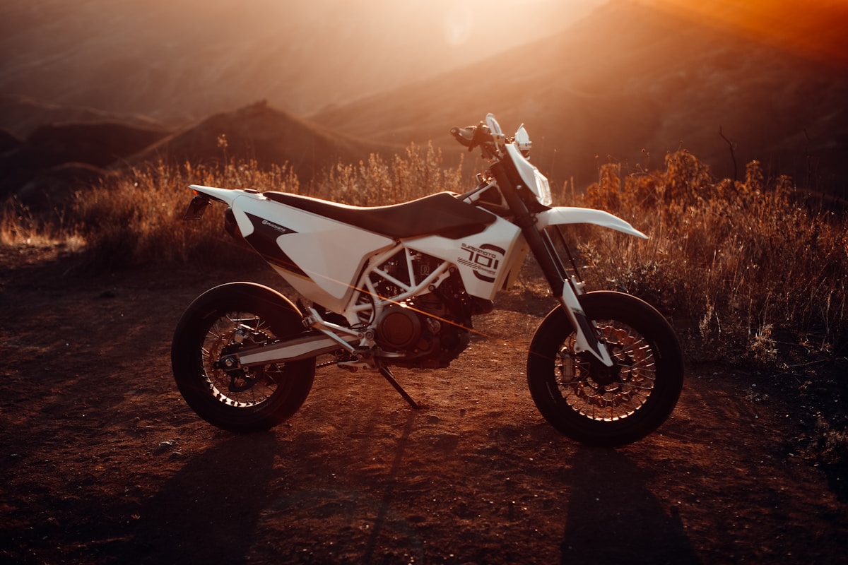 Moto tout-terrain blanche sur un chemin de terre au coucher de soleil.