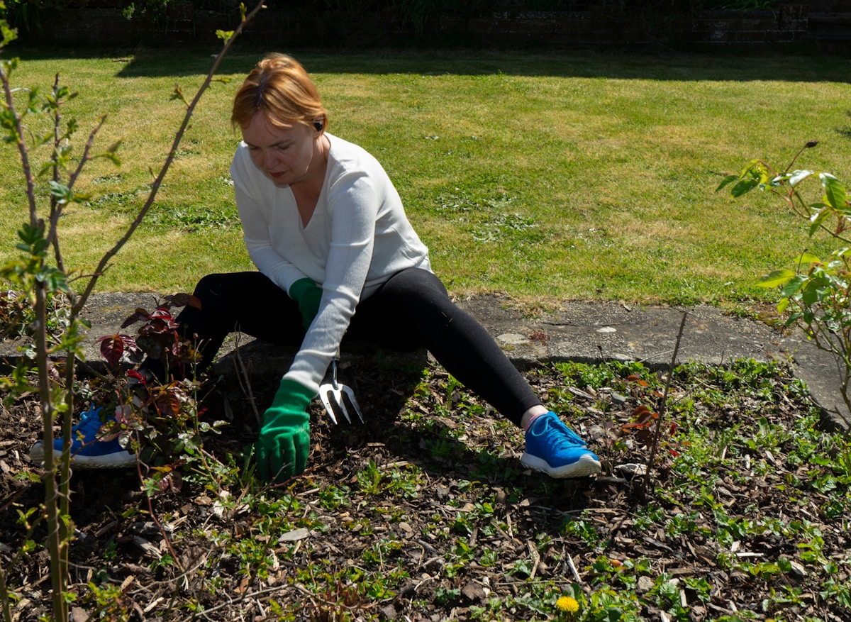 Femme en tenue de jardinage travaillant dans un jardin verdoyant.