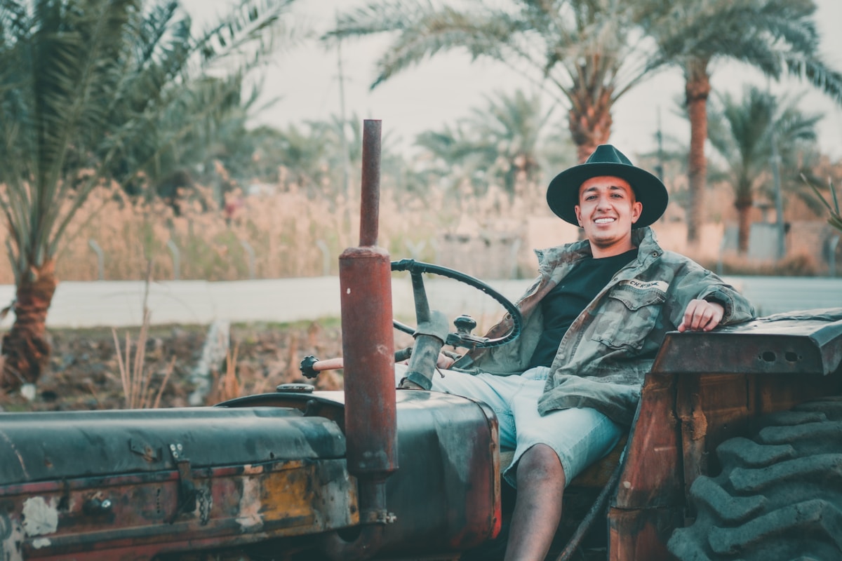 Homme souriant assis sur un tracteur vintage dans un paysage tropical.