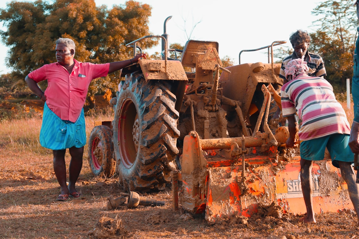 Deux personnes réparant un tracteur agricole dans un champ.