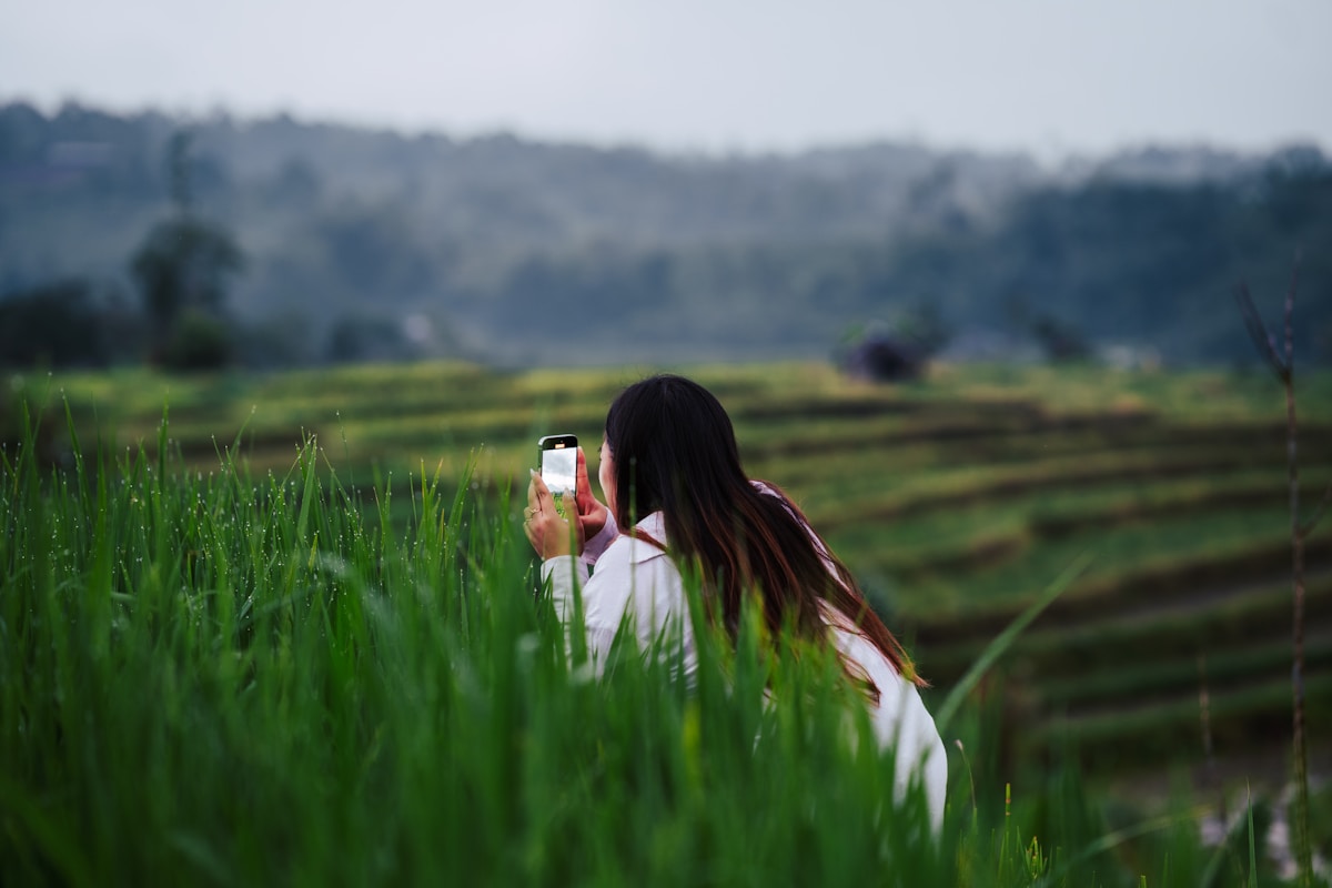 Femme photographiant un paysage verdoyant avec un téléphone portable.