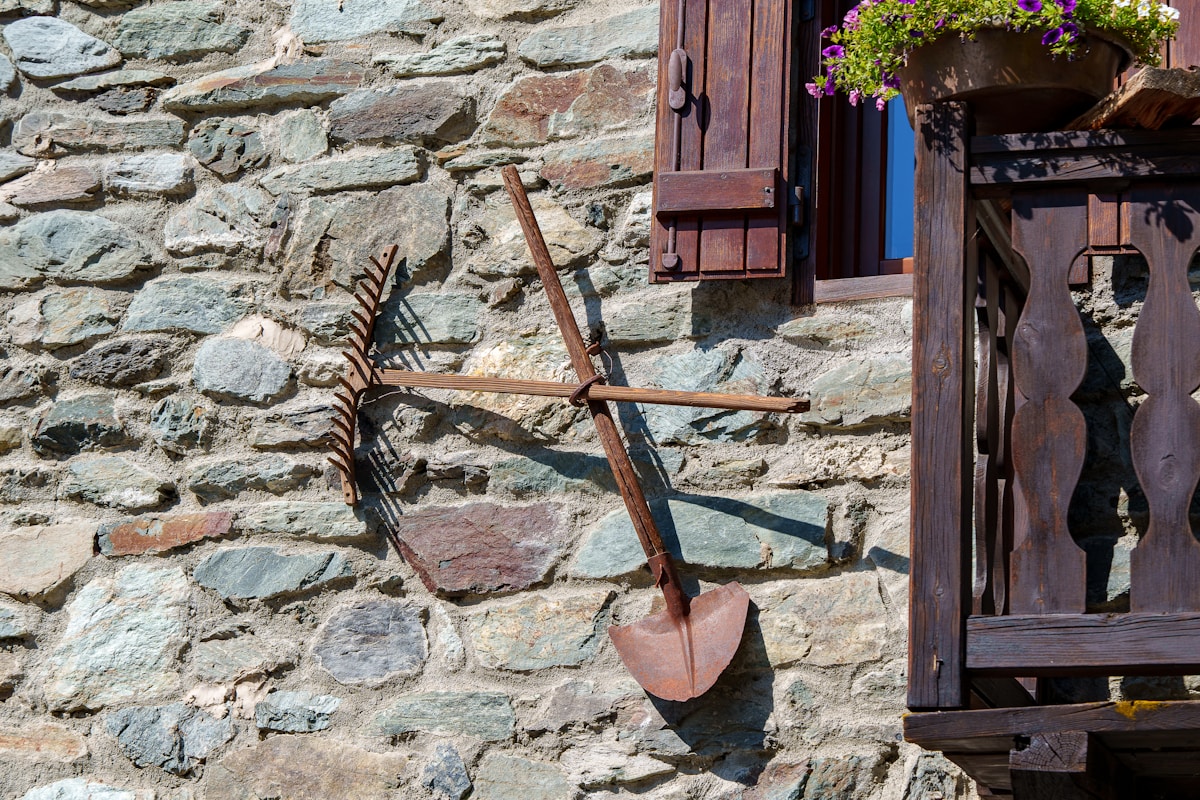 Vieux outils de jardinage accrochés sur un mur de pierre.