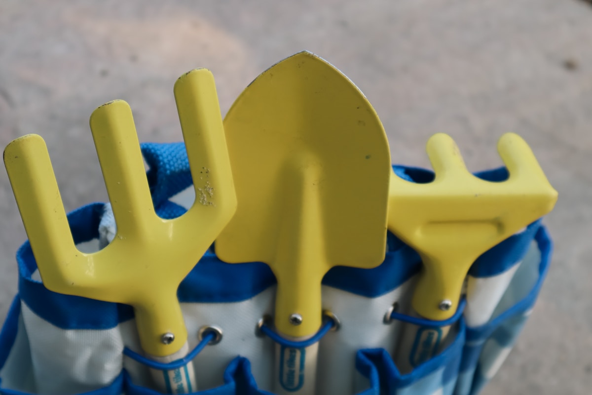 Outils de jardinage jaunes et bleus sur fond gris.